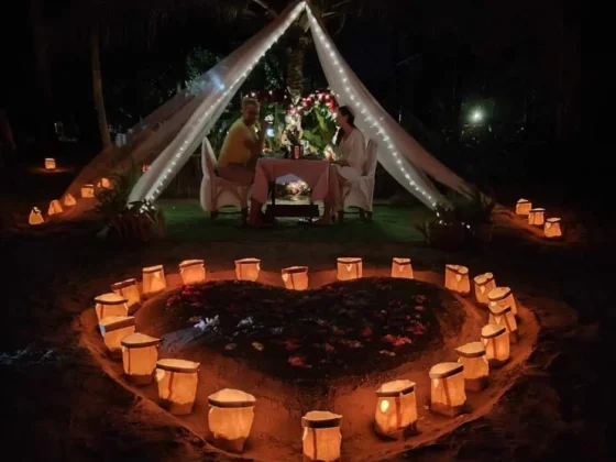 A tent at night inside a heart of lit paper lanterns on the sand