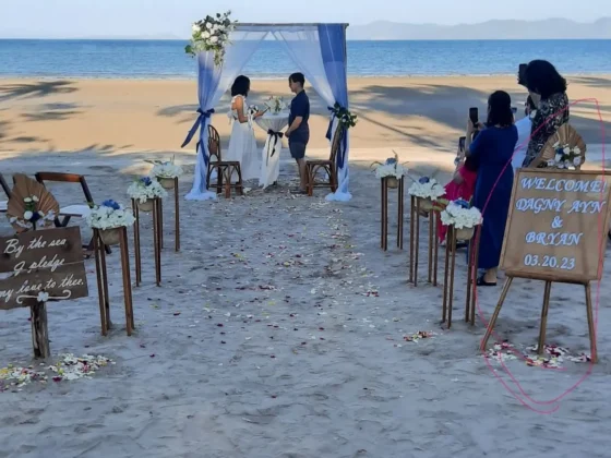 A beach wedding ceremony under a white and blue arch at the waterline