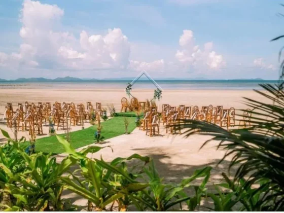 Rows of wooden chairs on the lawn facing an arch by the beach