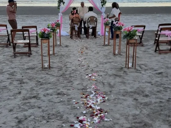 A rose-petal aisle across the sand to a wedding arch at the water